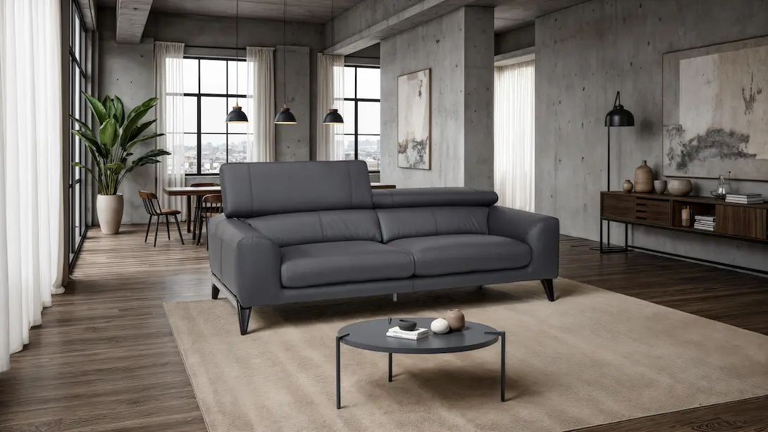 Sofá de dos plazas tapizado en piel gris antracita con cabeceros ajustables en sala estilo industrial de planta abierta con piso de madera oscura